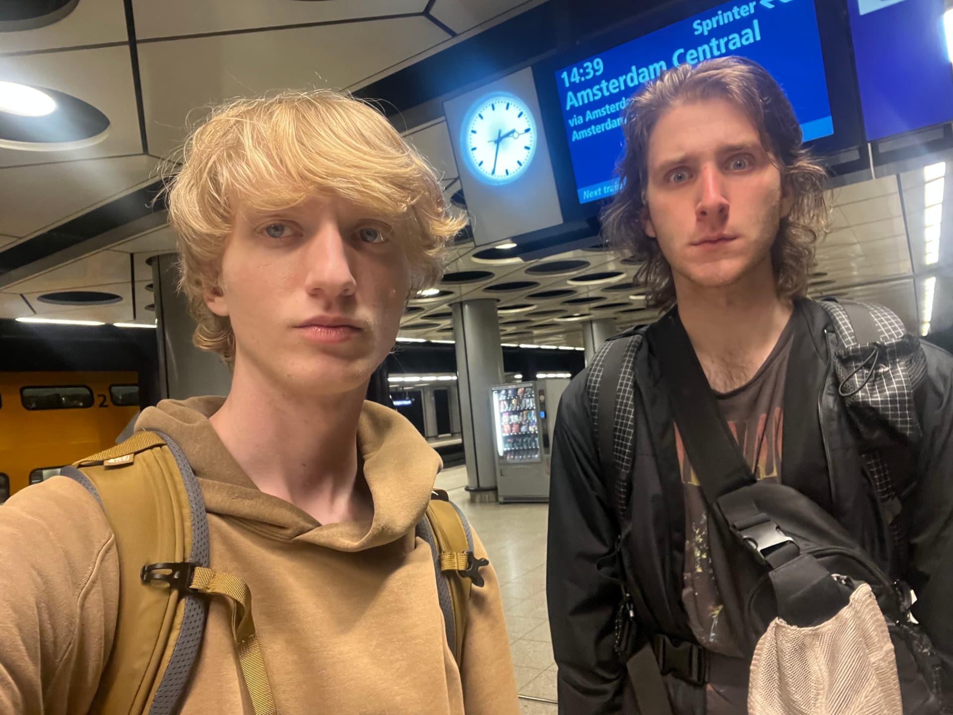 Two backpackers on a train platform at Schiphol, waiting for the Sprinter to Amsterdam Centraal